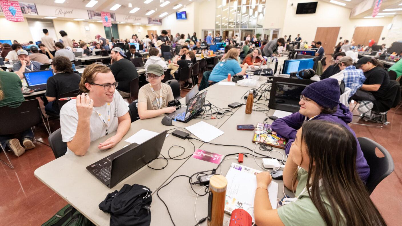 Students sit at tables with laptops during a gaming competition.