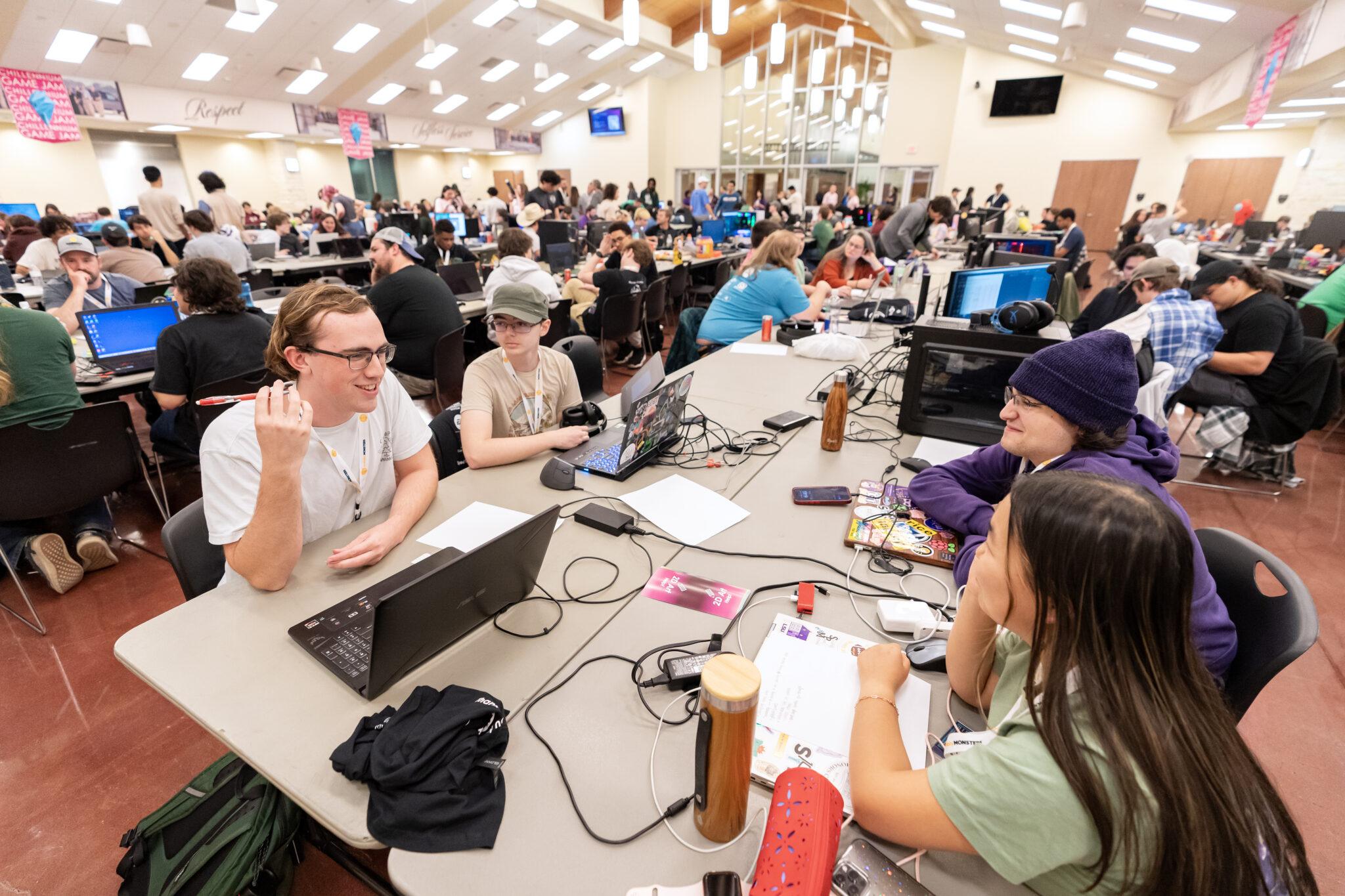 Students sit at tables with laptops during a gaming competition.