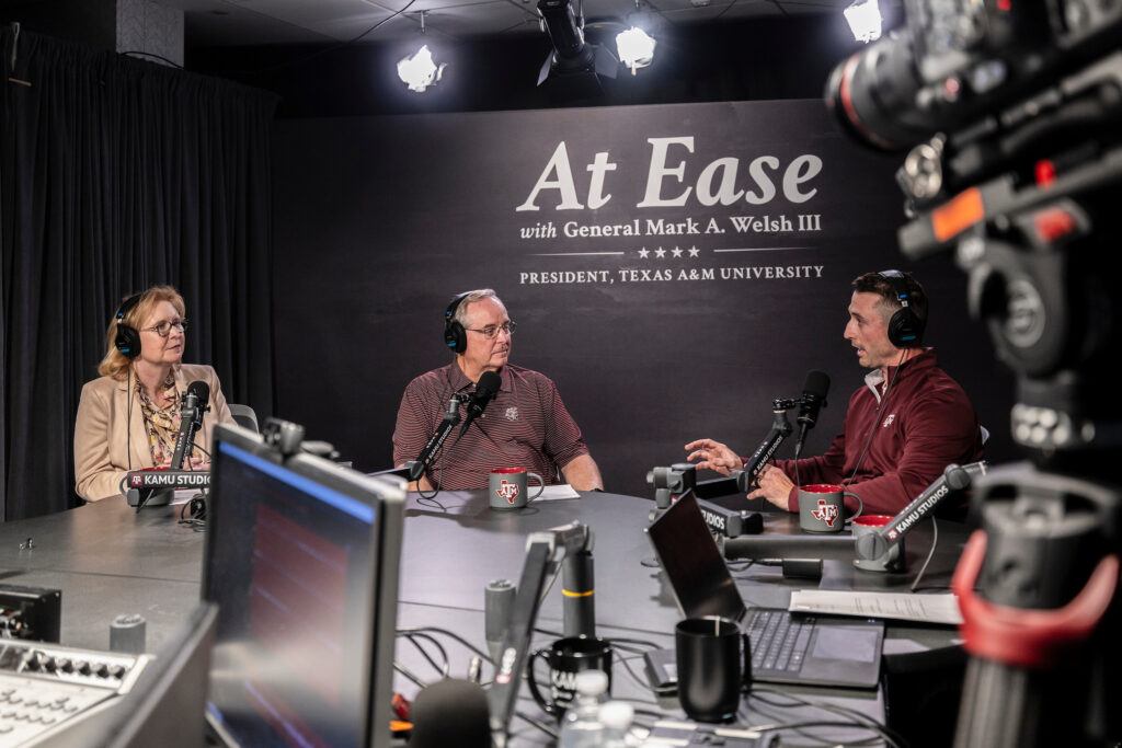 Three people recording a podcast in a studio surrounded with computer equipment, microphones and cameras.