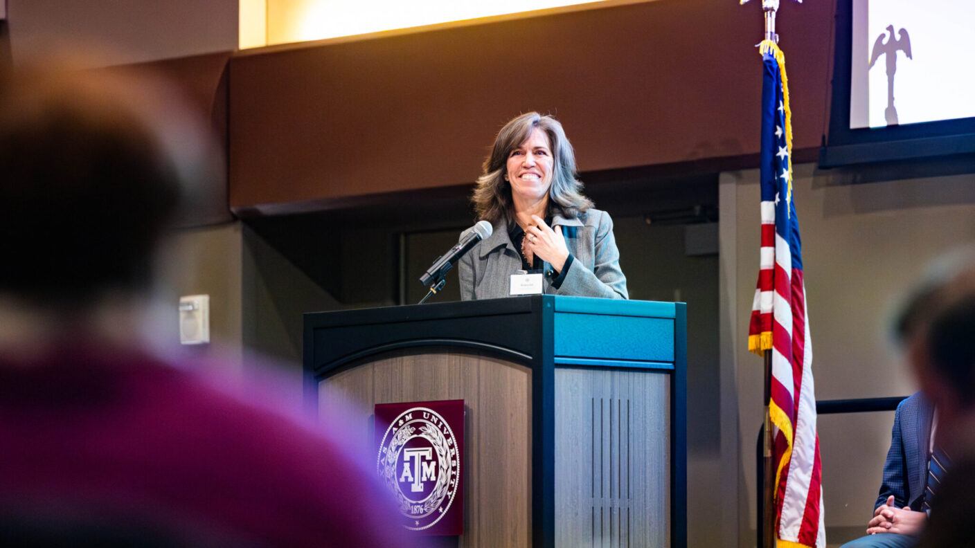 A woman stands at a podium next to the American flag