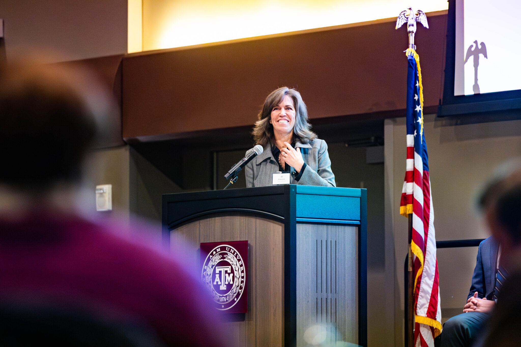 A woman stands at a podium next to the American flag