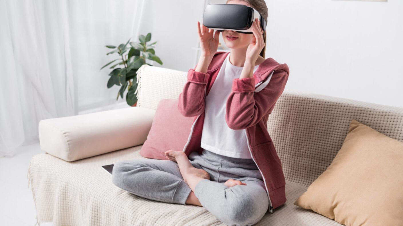 A woman sitting on a couch while wearing a virtual reality headset.