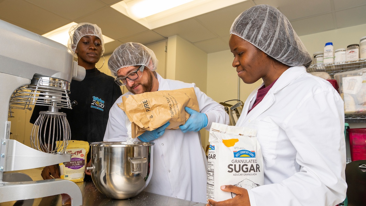 Food science students pour flour into a large mixing bowl