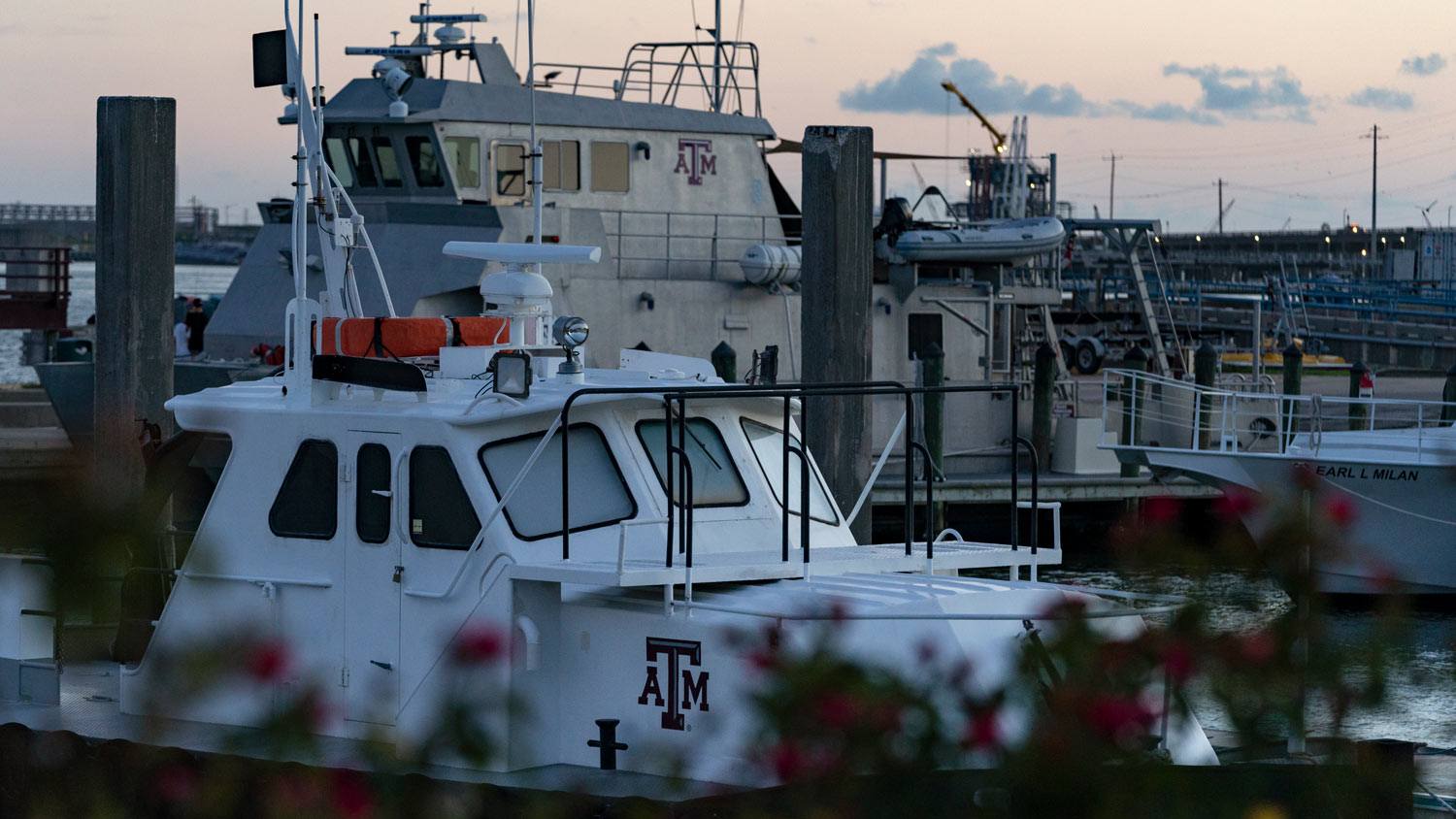 A boat and a ship, both with Texas A&M logos, docked in the Galveston marina