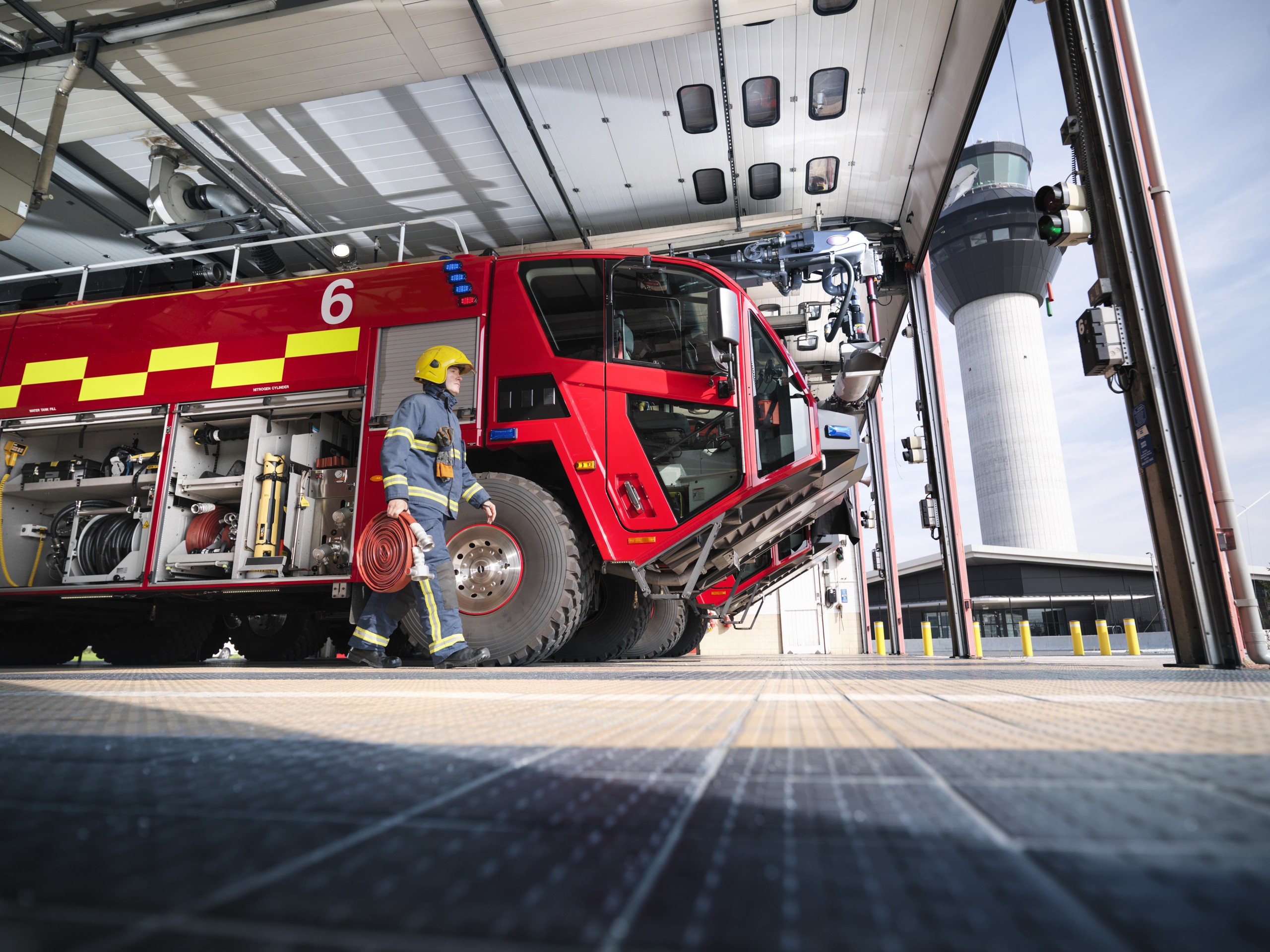 A photo of a firefighter carrying equipment to a fire engine in an airport fire station.