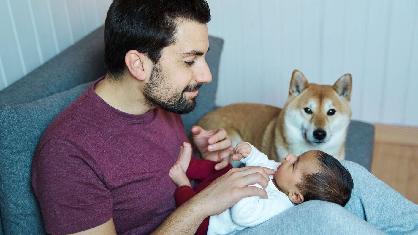 a dad holding a baby with a dog watching