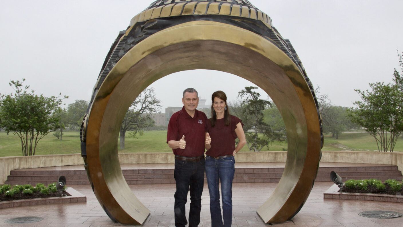 A photo of a man and woman standing under the Aggie Ring replica at The Association of Former Students