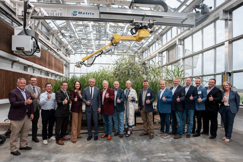 A photo of a group of people standing in a greenhouse on the Texas A&M University campus.
