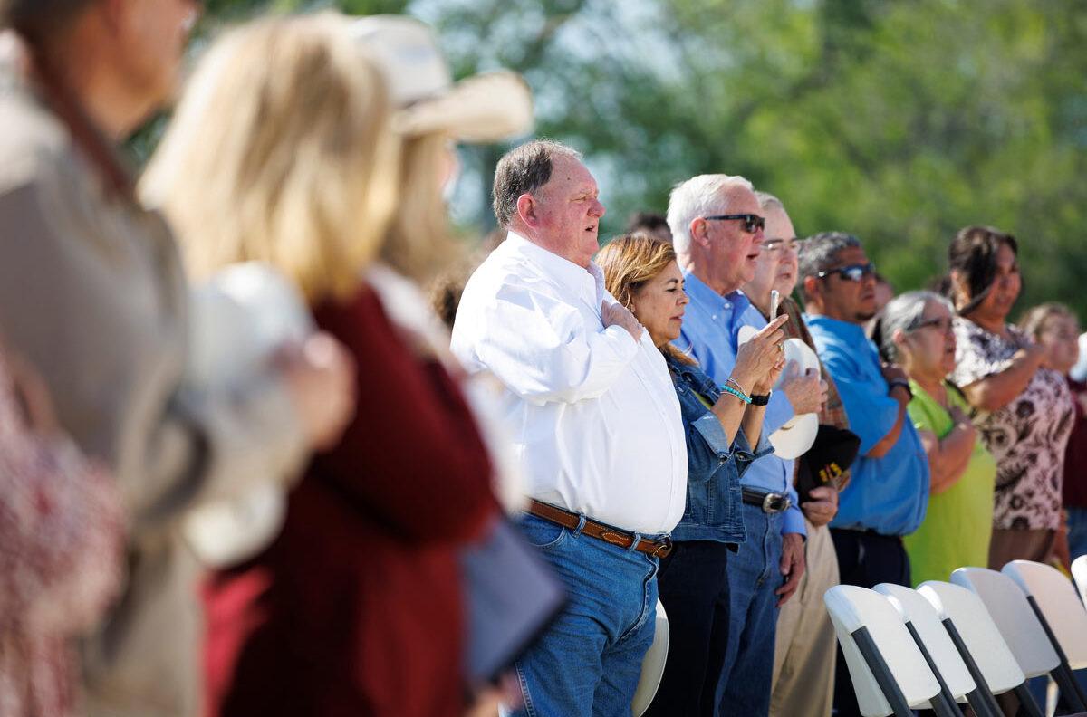 Community members with their hands on their hearts at the opening of the Kenedy County Medical Clinic ribbon cutting ceremony