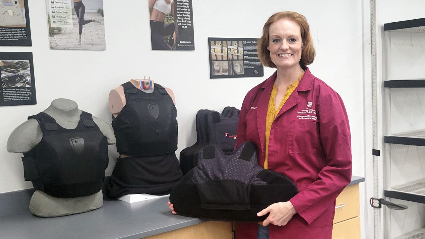 A photo of a woman in a lab coat posting with ballistic vests that were designed for women.