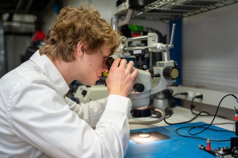 A photo of a person in a white shirt looking through a microscope.
