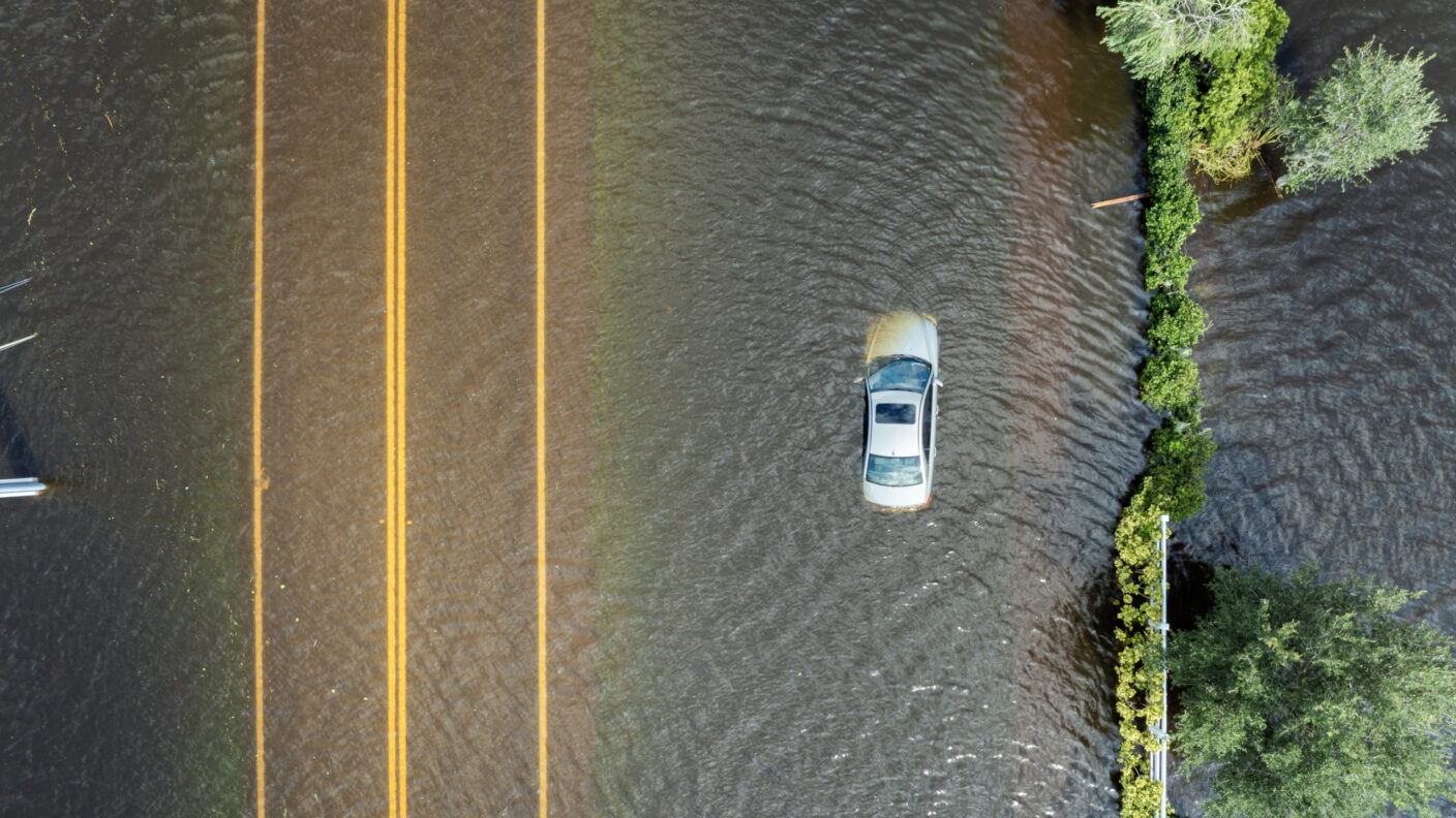 An aerial photo of a car submerged in water next to a road.