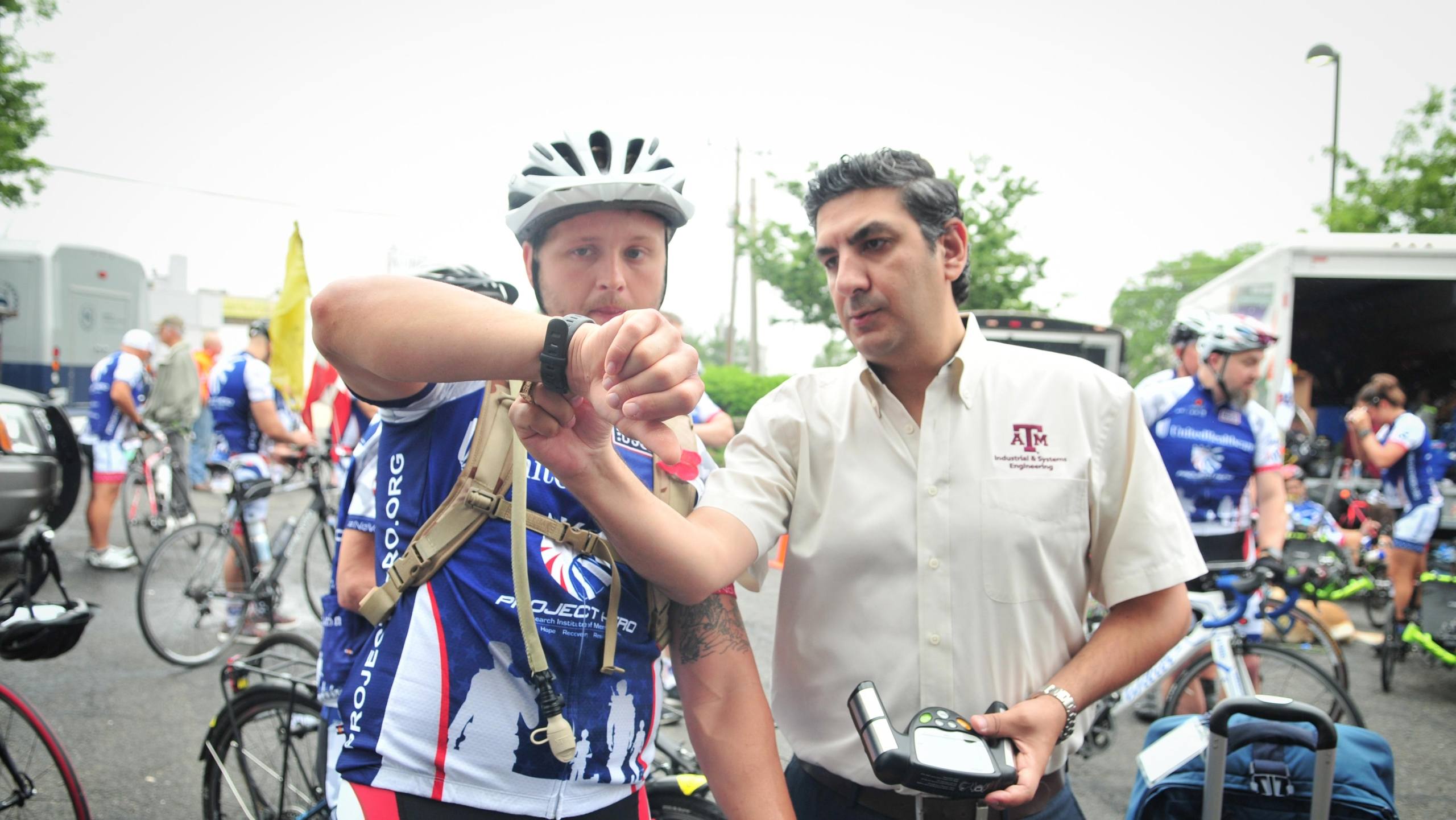 A photo of a man checking a device on the wrist of a cyclist prior to a cycling event.