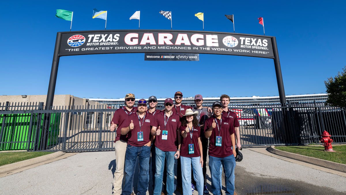 Nine Aggie students pose in front of the Texas Motor Speedway Garage gate