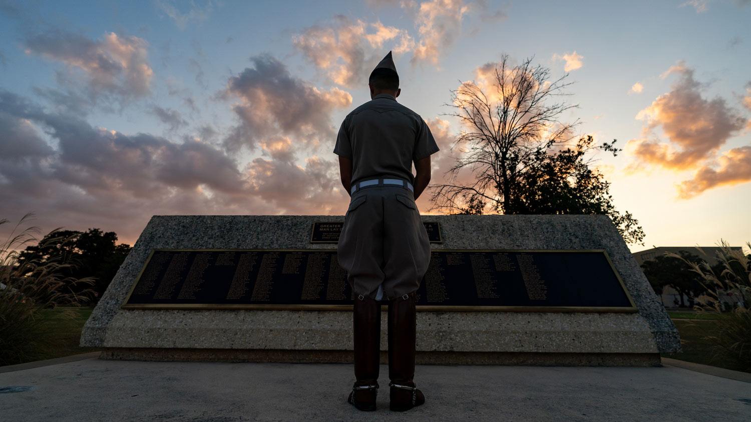 A silhouette of a cadet reading a campus war memorial in the sunrise
