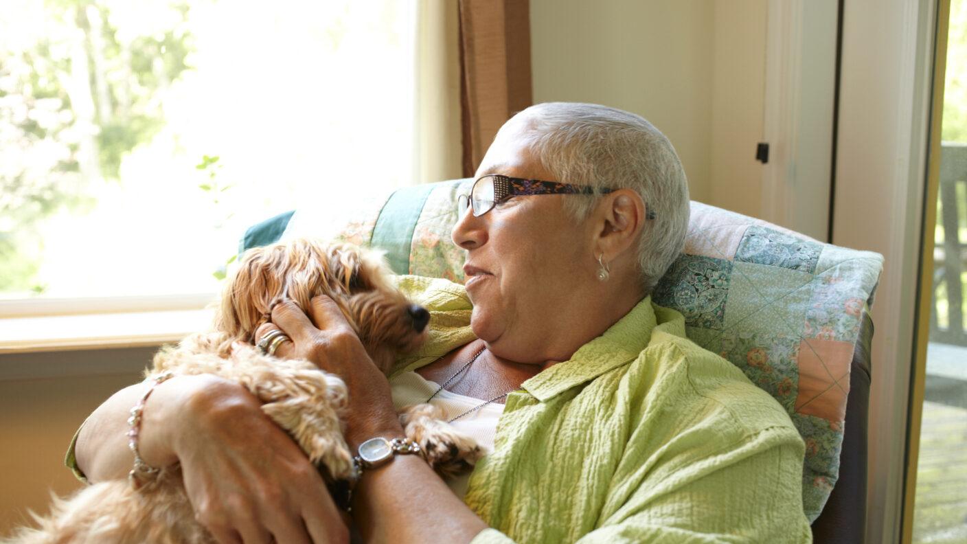 an older adult woman cuddling a small dog on her lap in a living room