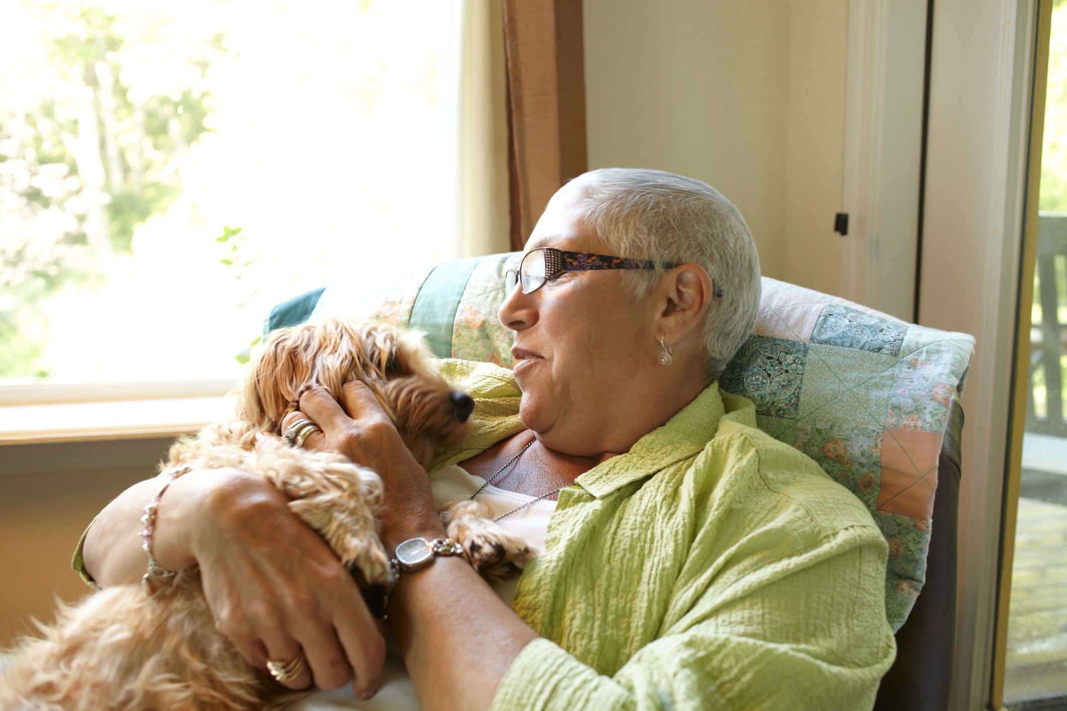 an older adult woman cuddling a small dog on her lap in a living room