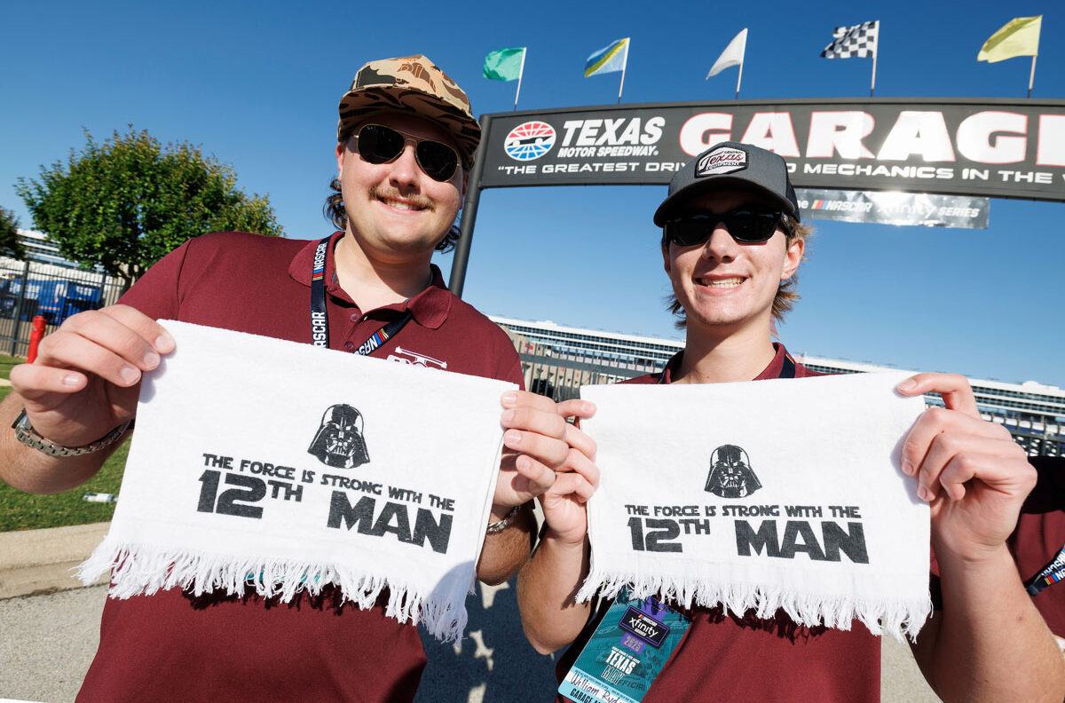 Two Aggie Students hold up Star Wars-themed 12th Man towels in front of the Texas Motor Speedway Garage sign