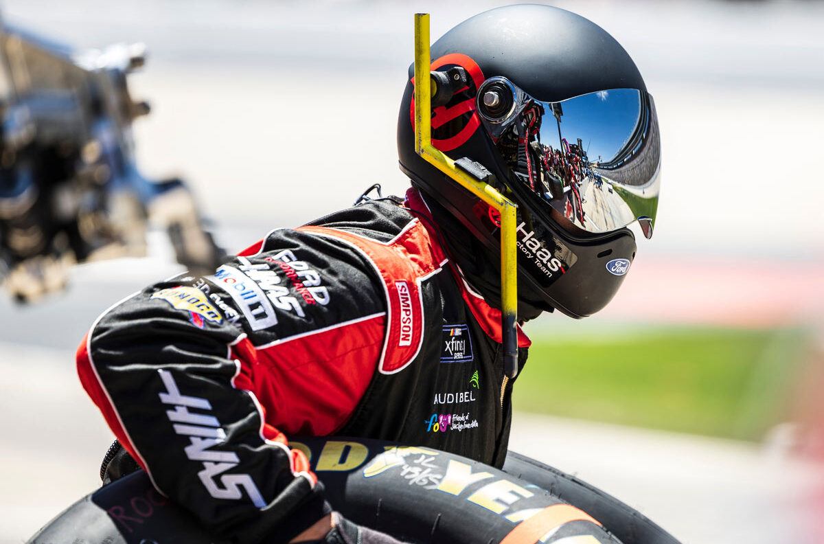 A pit crew member wearing a masked helmet poised to replace a tire during a pitstop