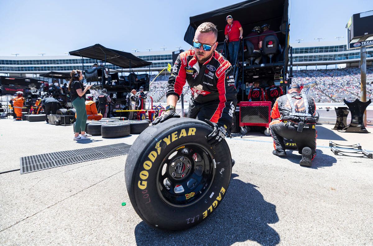 A pit crew member rolls out a spare tire