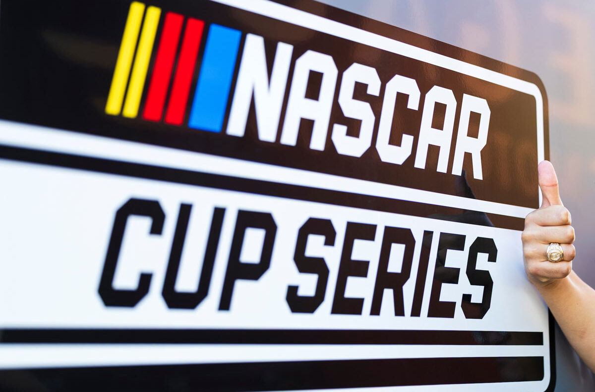 A Gig 'Em wearing an Aggie ring next to a NASCAR Cup Series sign