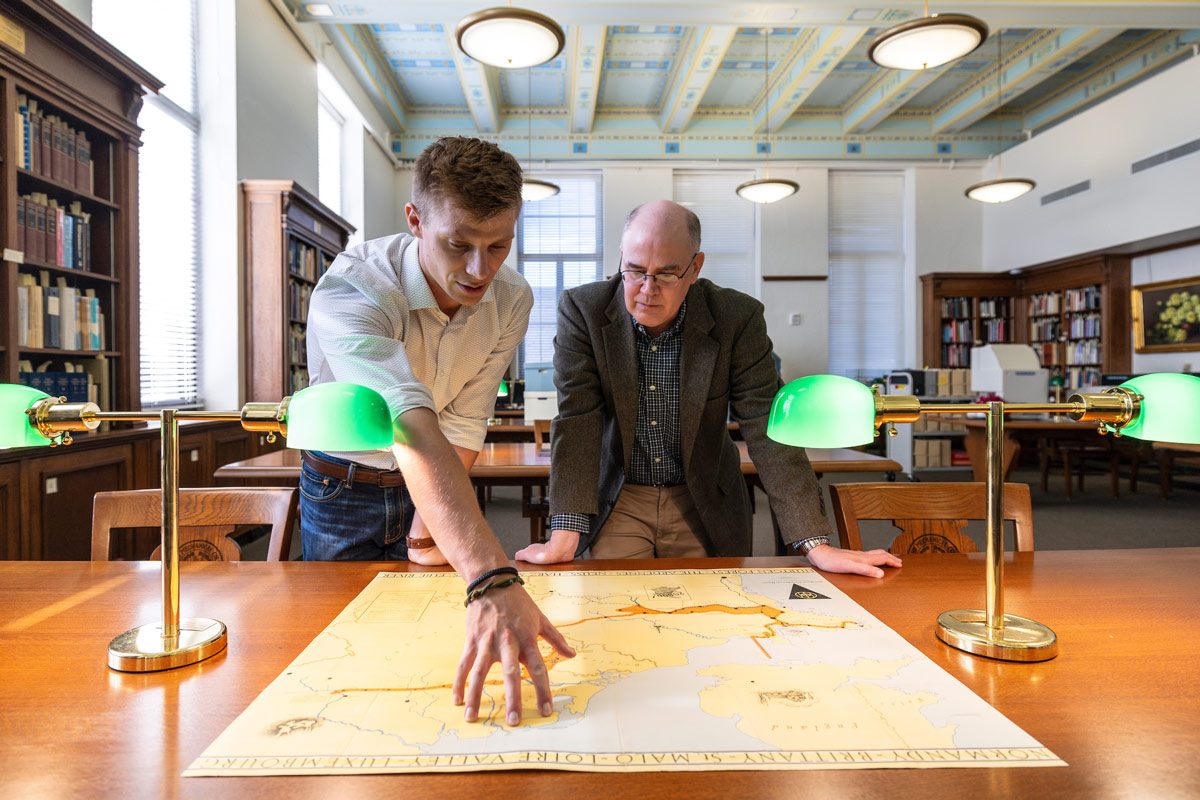 Tristan Krause and a Texas A&M professor study a large map
