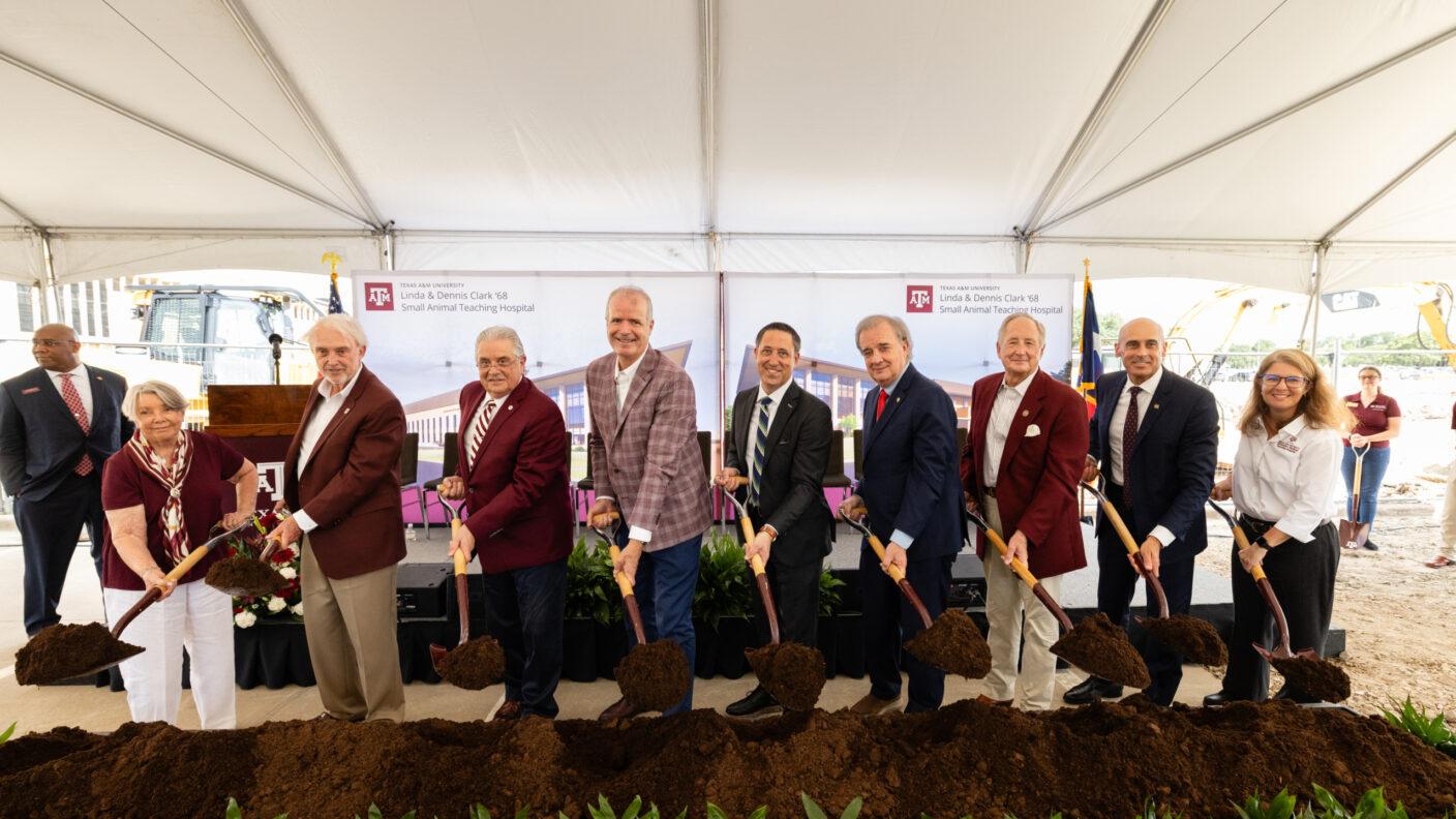A photo of a group of people standing under a tent with shovels of dirt during a groundbreaking event.