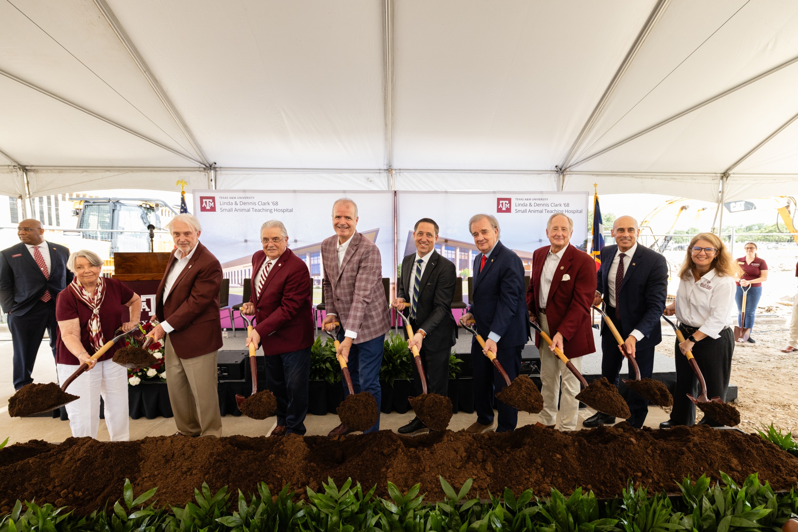 A photo of a group of people standing under a tent with shovels of dirt during a groundbreaking event.