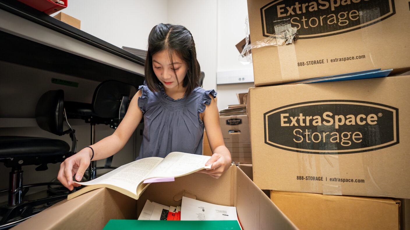 A female student sits on the floor of an office among stacks of boxes as she looks through donated papers