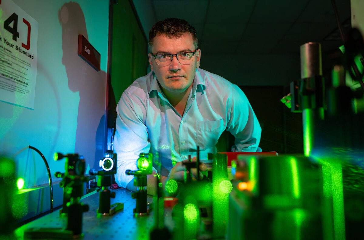 A photo of a researcher in a lab with devices illuminating green light.