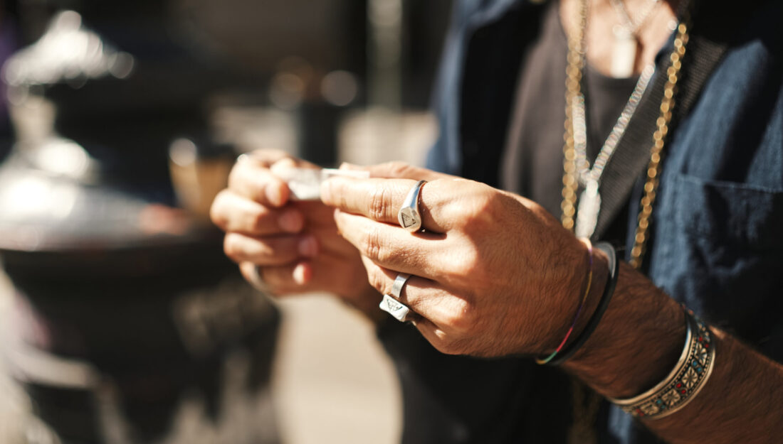 Close-up of male hands in bracelets and rings rolls cigarette. Male hands wrapping tobacco in tissue paper