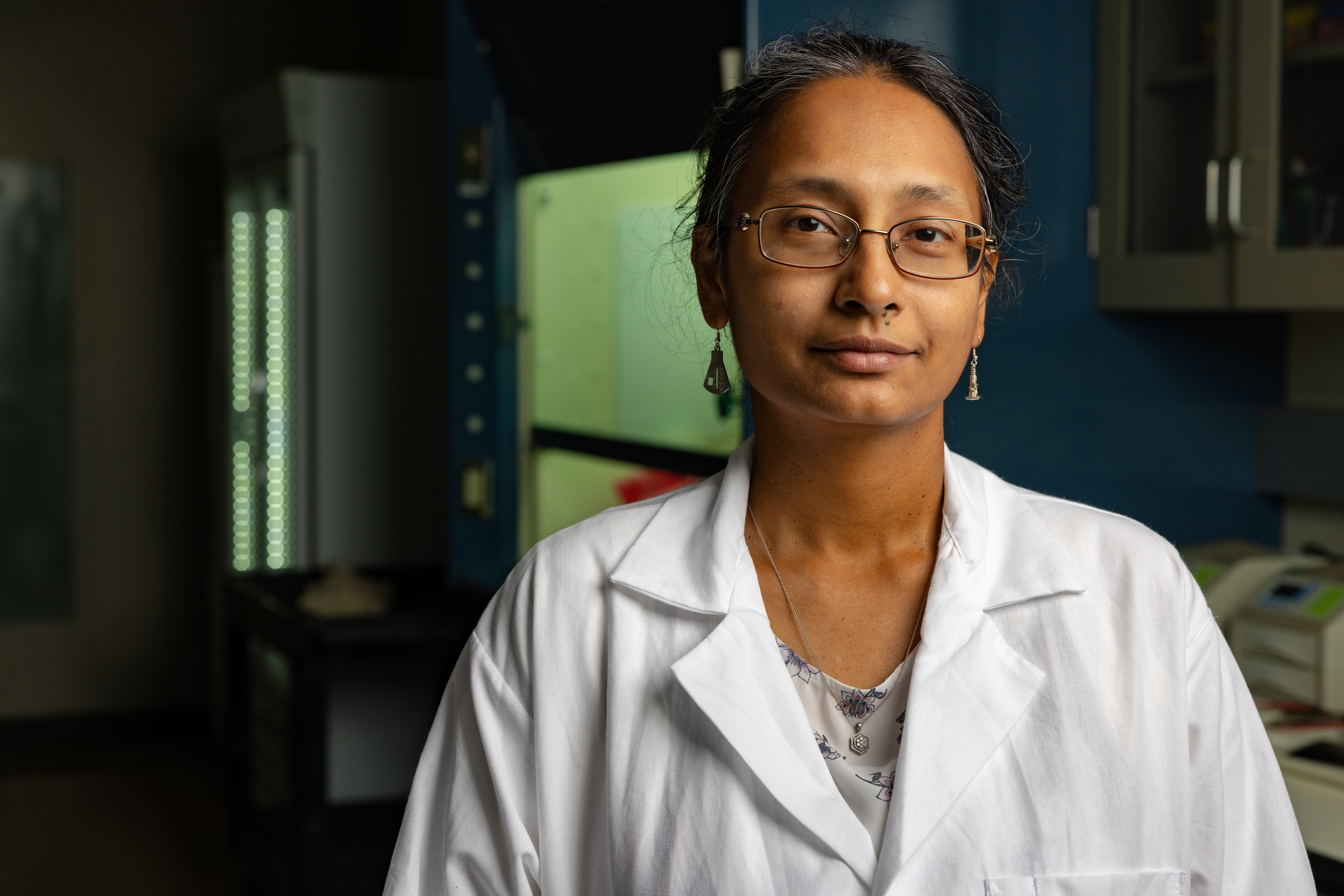 A photop of a researcher wearing a lab coat in a darkened lab.
