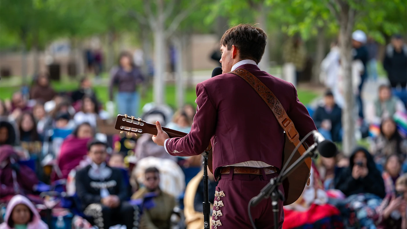 Mariachi member playing a guitar and singing performs in front of an audience in Aggie Park