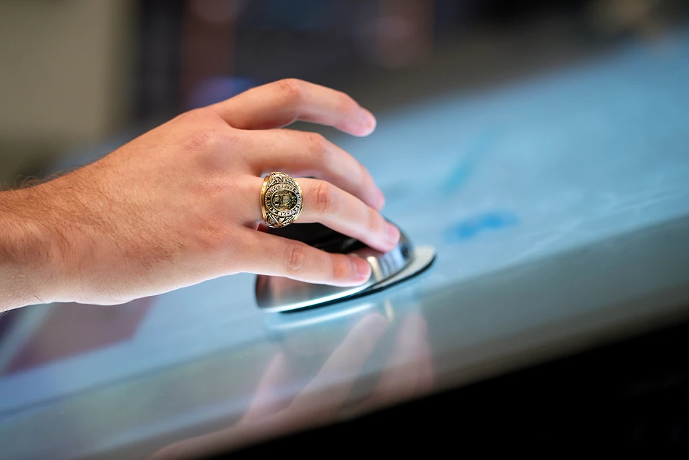 A hand wearing an Aggie ring interacts with a touch screen