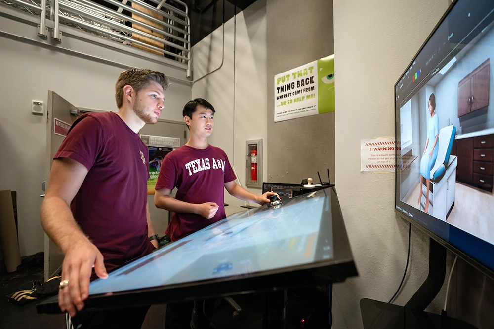 Two students interact with a touch screen to manipulate a 3D model used in VR trainings