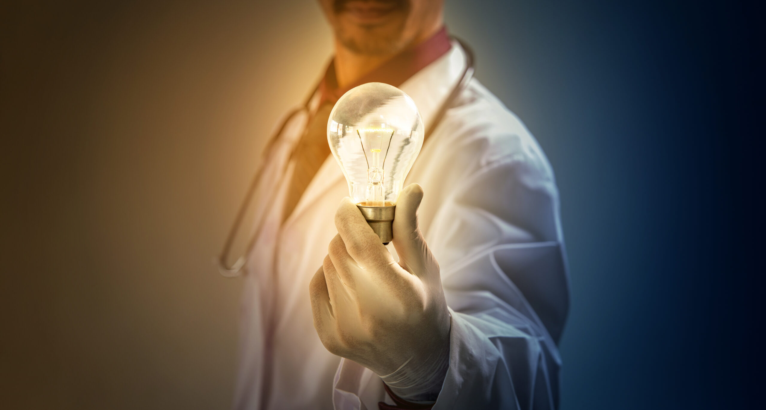 A photo of a man with a stethoscope and doctor's coat holding an illuminated light bulb.