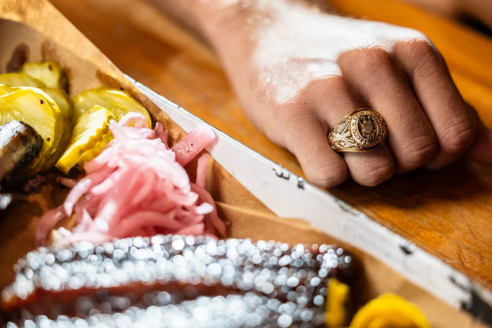 Hand with Aggie Ring on next to tray of barbecue