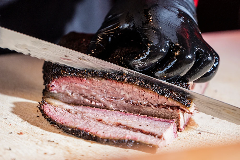 Person wearing black gloves and slicing brisket