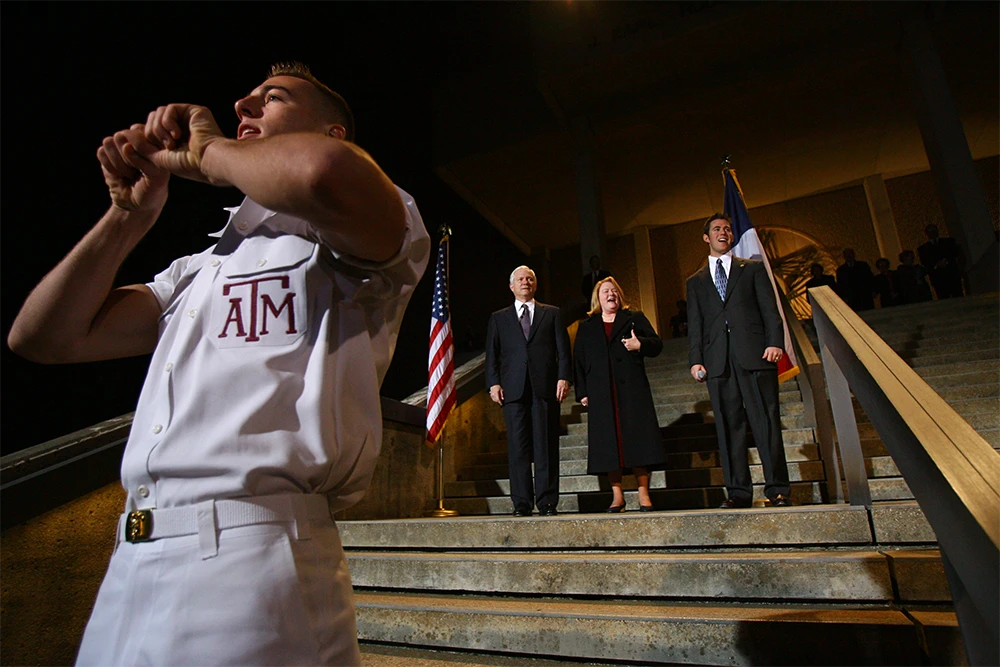 A Yell Leader stands in front of Robert and Becky Gates as he leads the gathered crowd in a yell