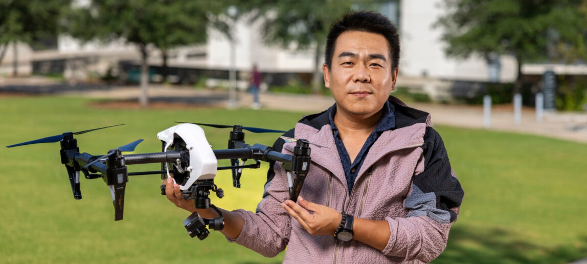 Dr. Dingding Ren holds a drone equipped with a thermal camera while standing outdoors in daylight.