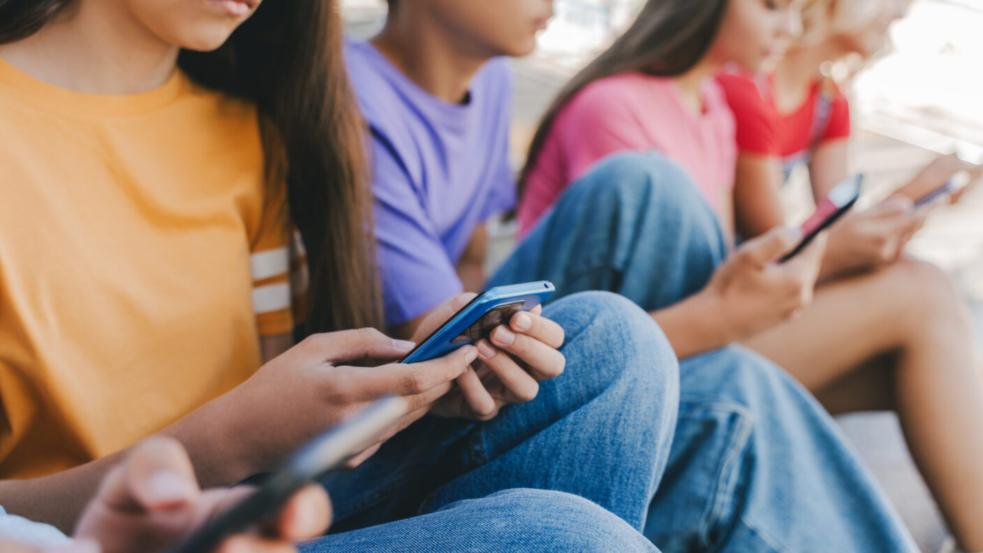 A group of teenagers sitting together while being focused on their phones.