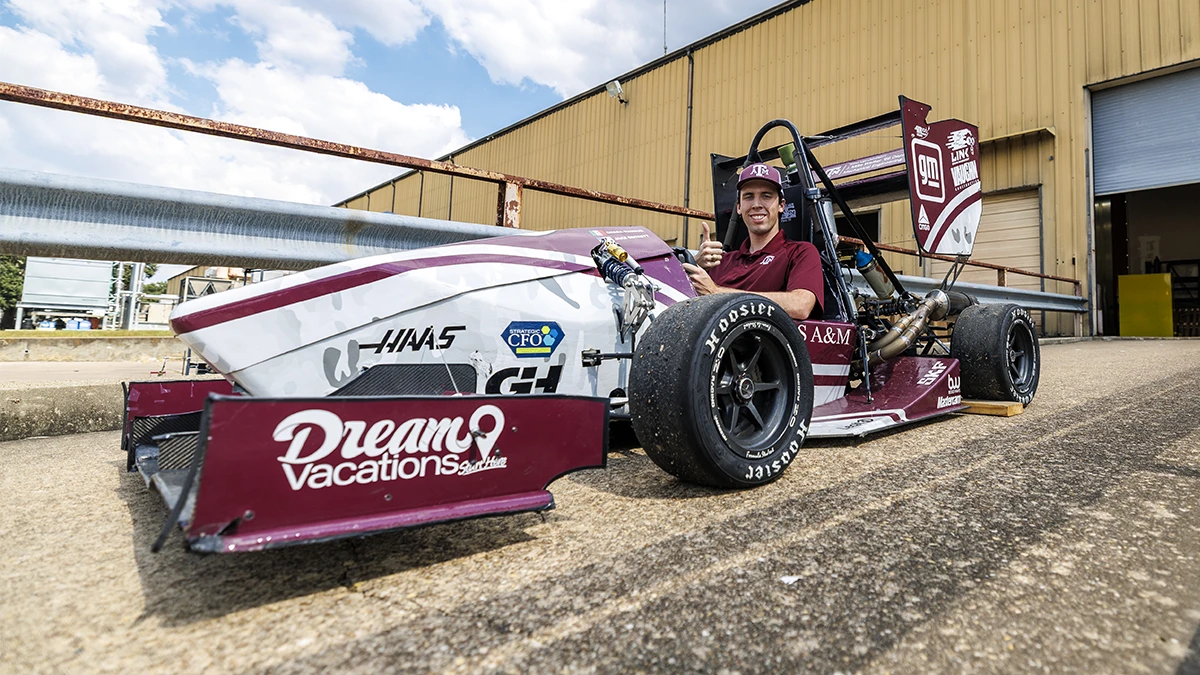 An Aggie gives a Gig 'Em in a Haas branded race car