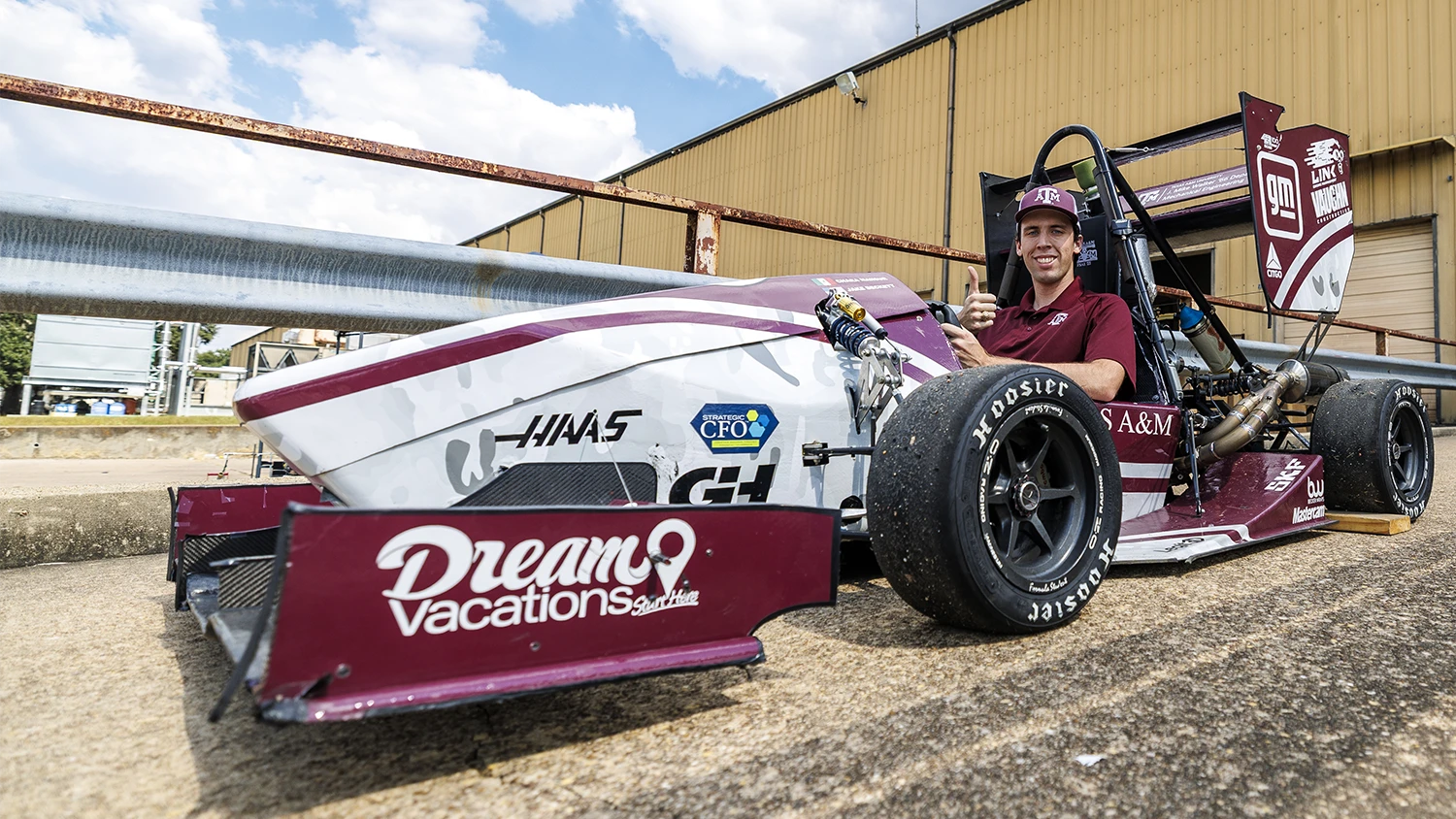 An Aggie gives a Gig 'Em in a Haas branded race car