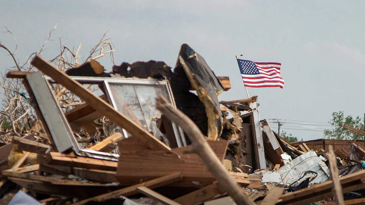 An American flag flies over rubble from a natural disaster