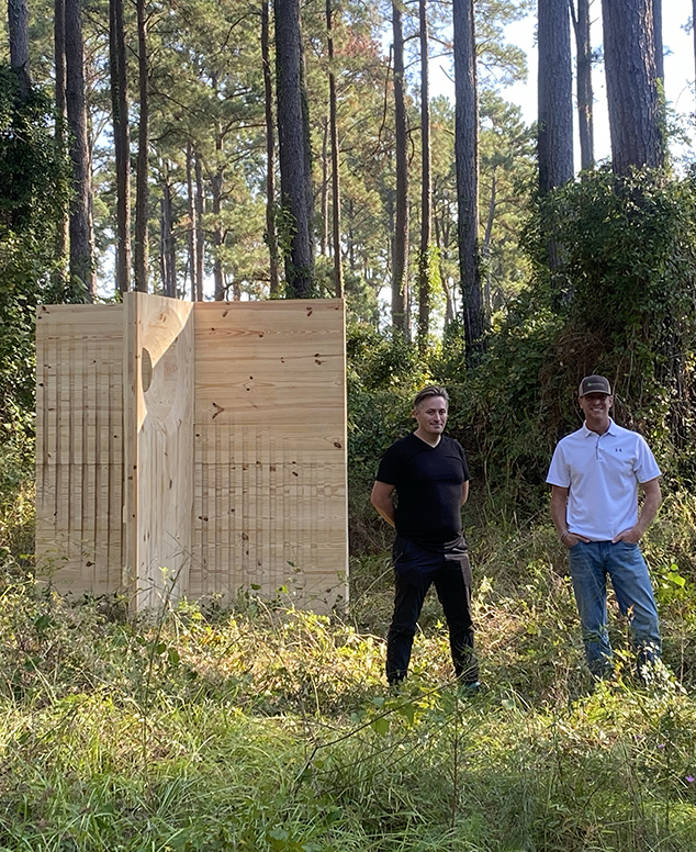 Tate and Stottlemyer standing in a forest next to a wall built of CLT