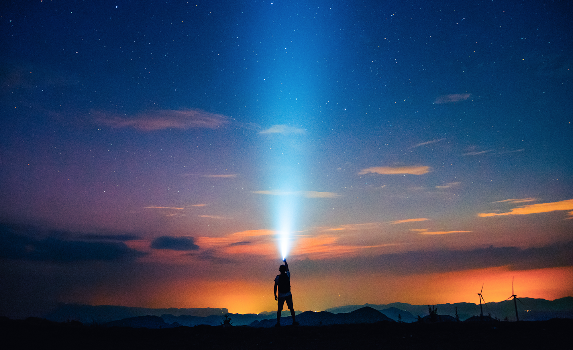 A photo of a person standing while holding a light as the sun sets in the background.