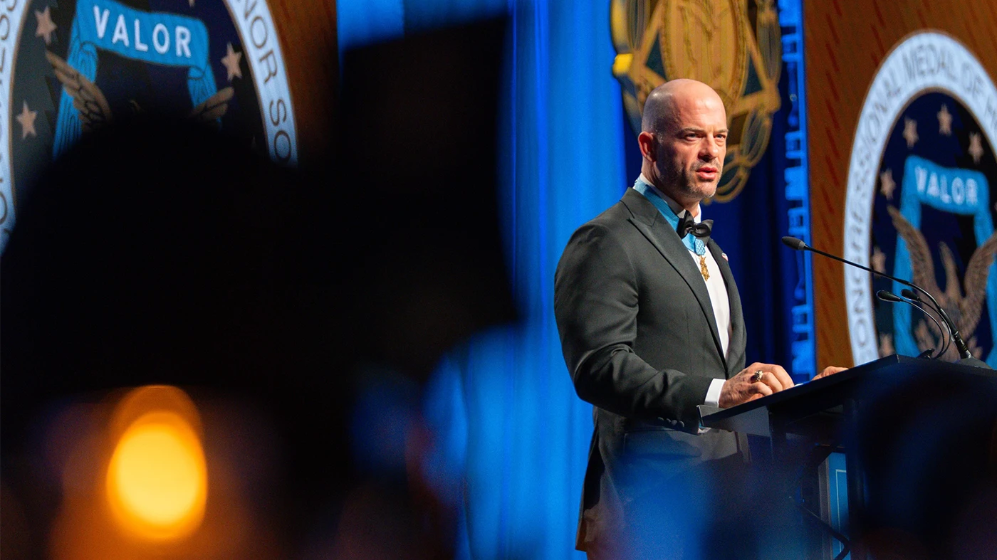 Matt Williams speaks at a podium while wearing his Medal of Honor