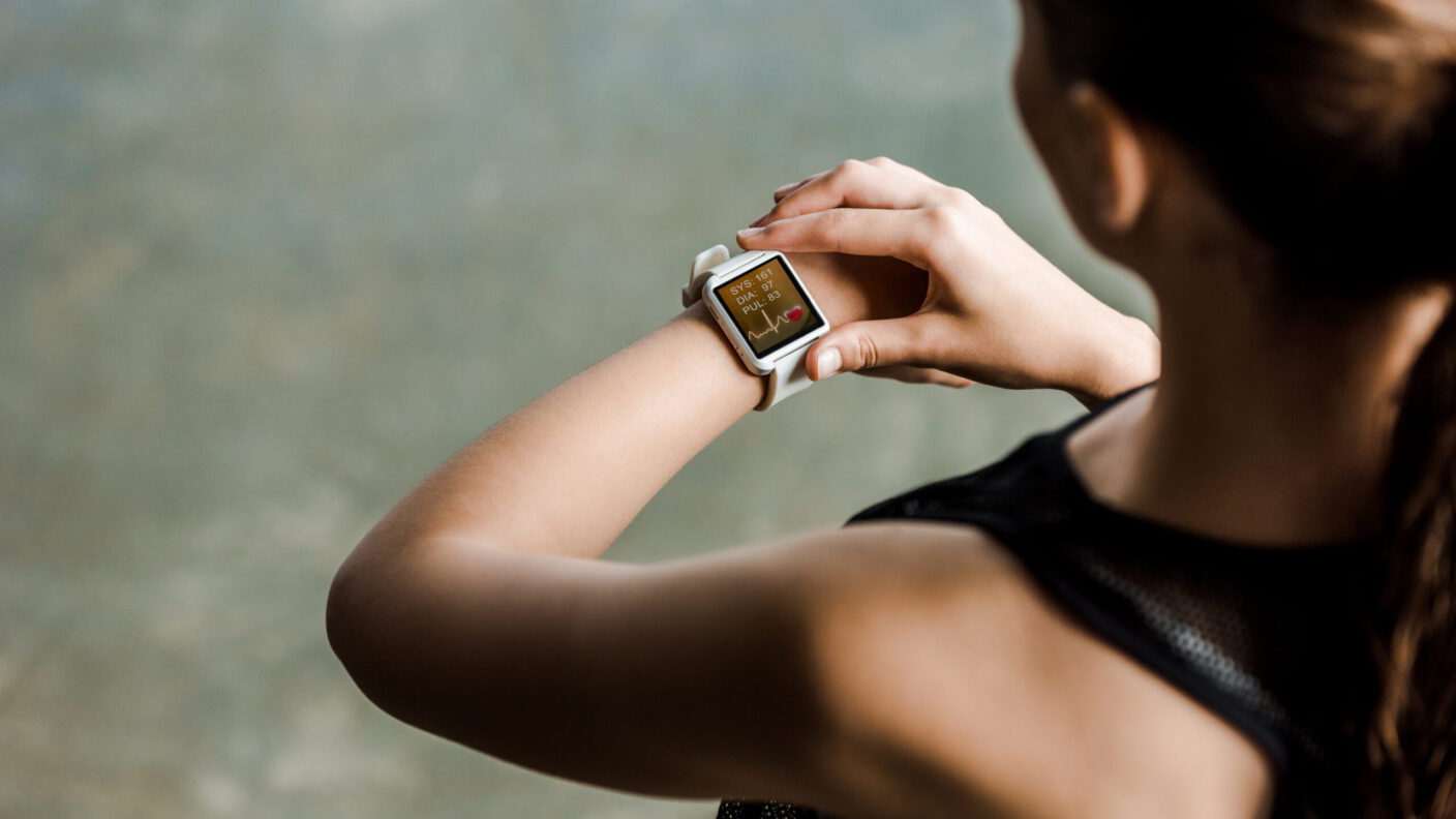 A photo looking over a woman's shoulder as she is looking at her smartwatch, which is displaying her heartbeat rate after a workout.