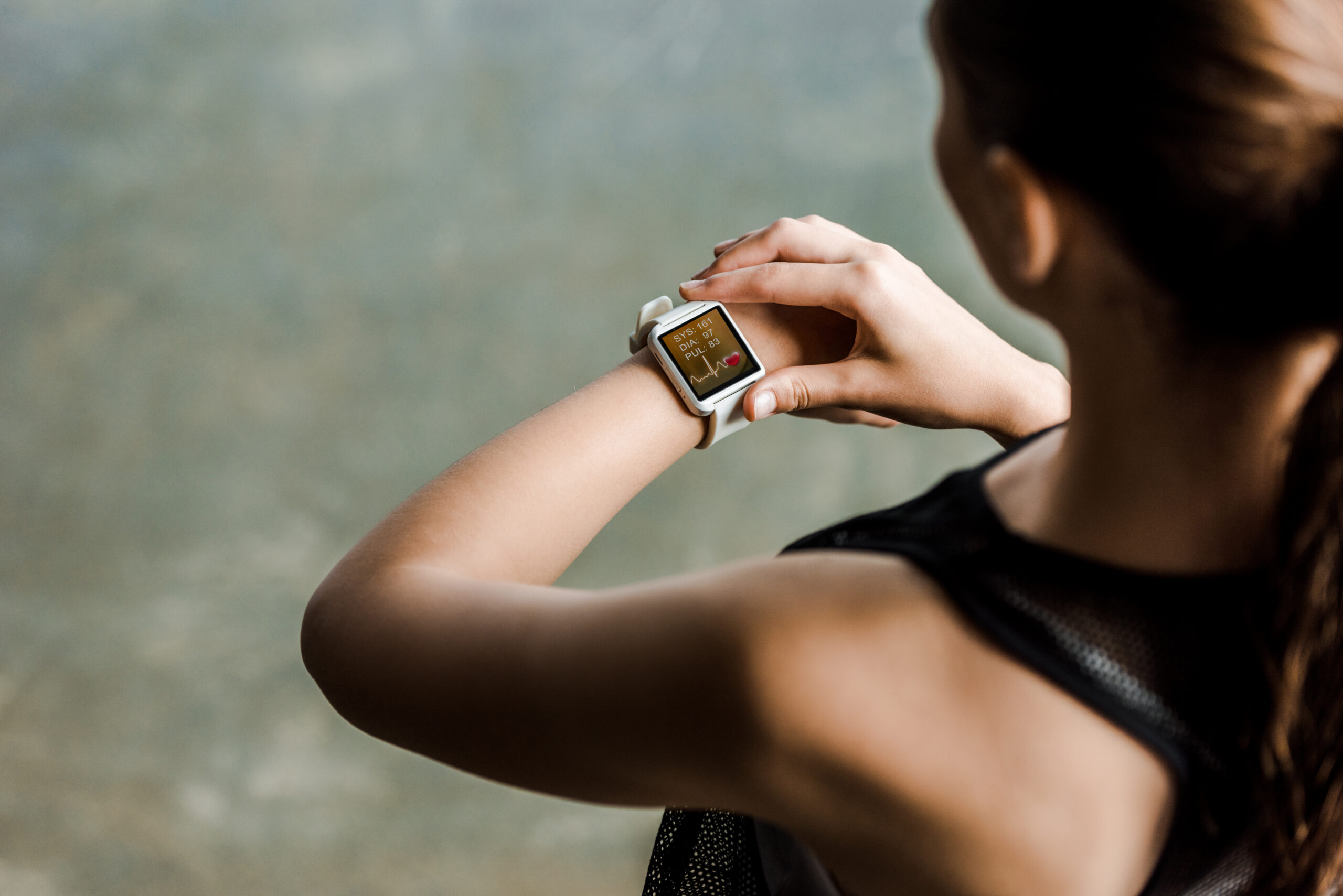 A photo looking over a woman's shoulder as she is looking at her smartwatch, which is displaying her heartbeat rate after a workout.