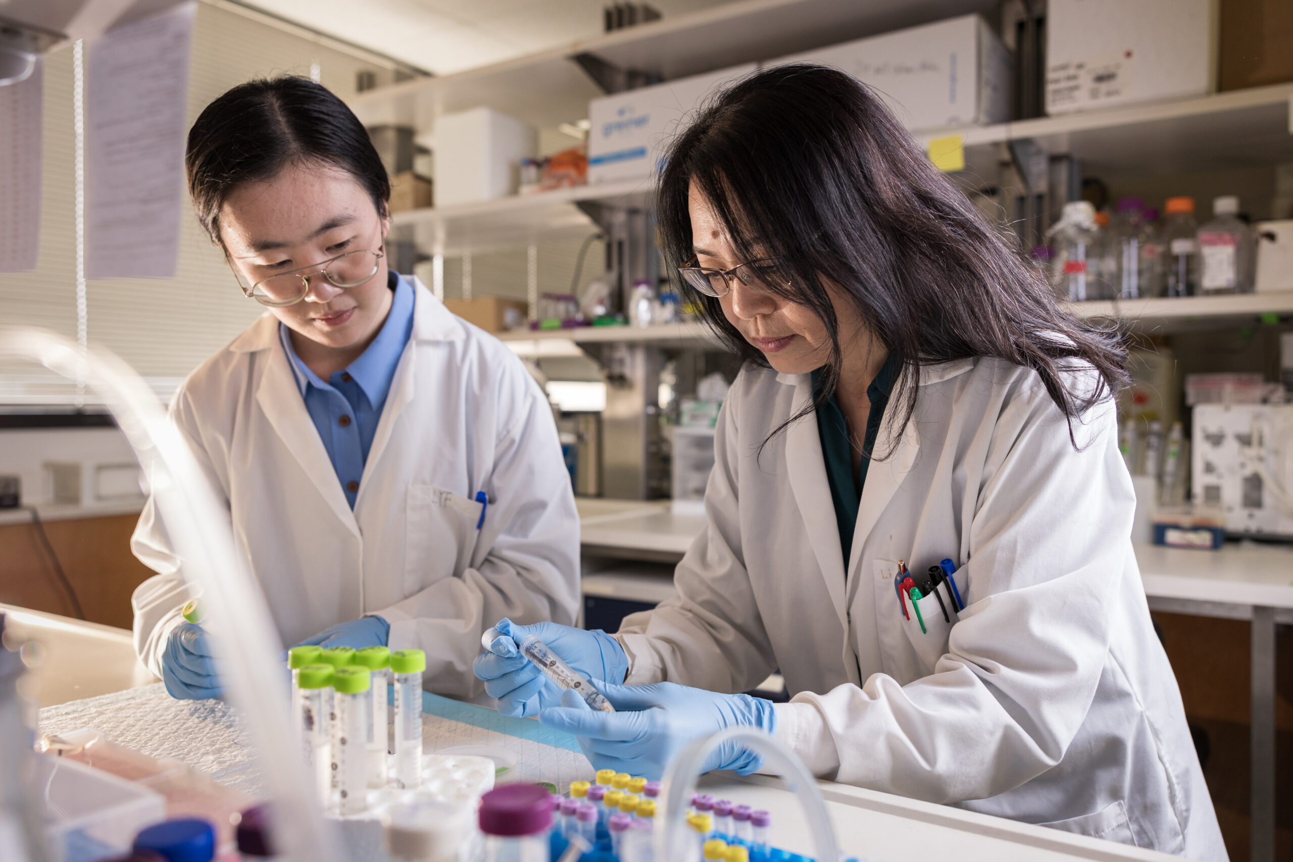 A photo of two women working in a lab with sample tubes while wearing lab coats.